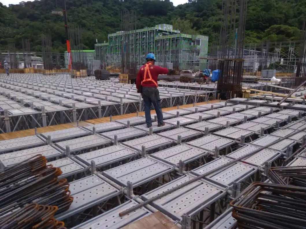 Inspirando sua Obra: Dicas de Construção, Reforma e Decoração: Operário da construção civil em um canteiro de obras, caminhando sobre estruturas metálicas com lajes e formas de concreto, ao fundo há armaduras e estruturas em andamento.